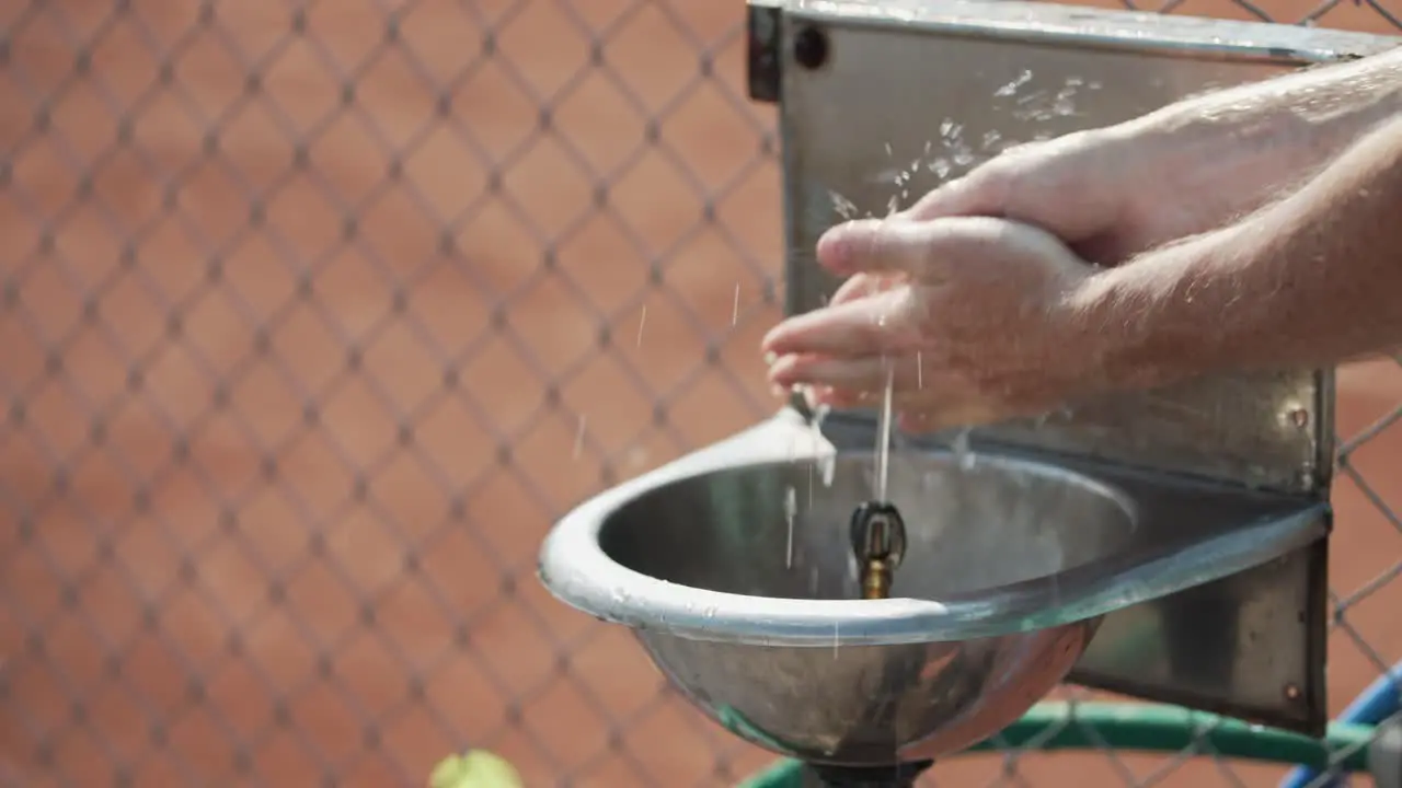 Slow motion closeup of man washing hands in stainless steel sink with water spurting from spigot