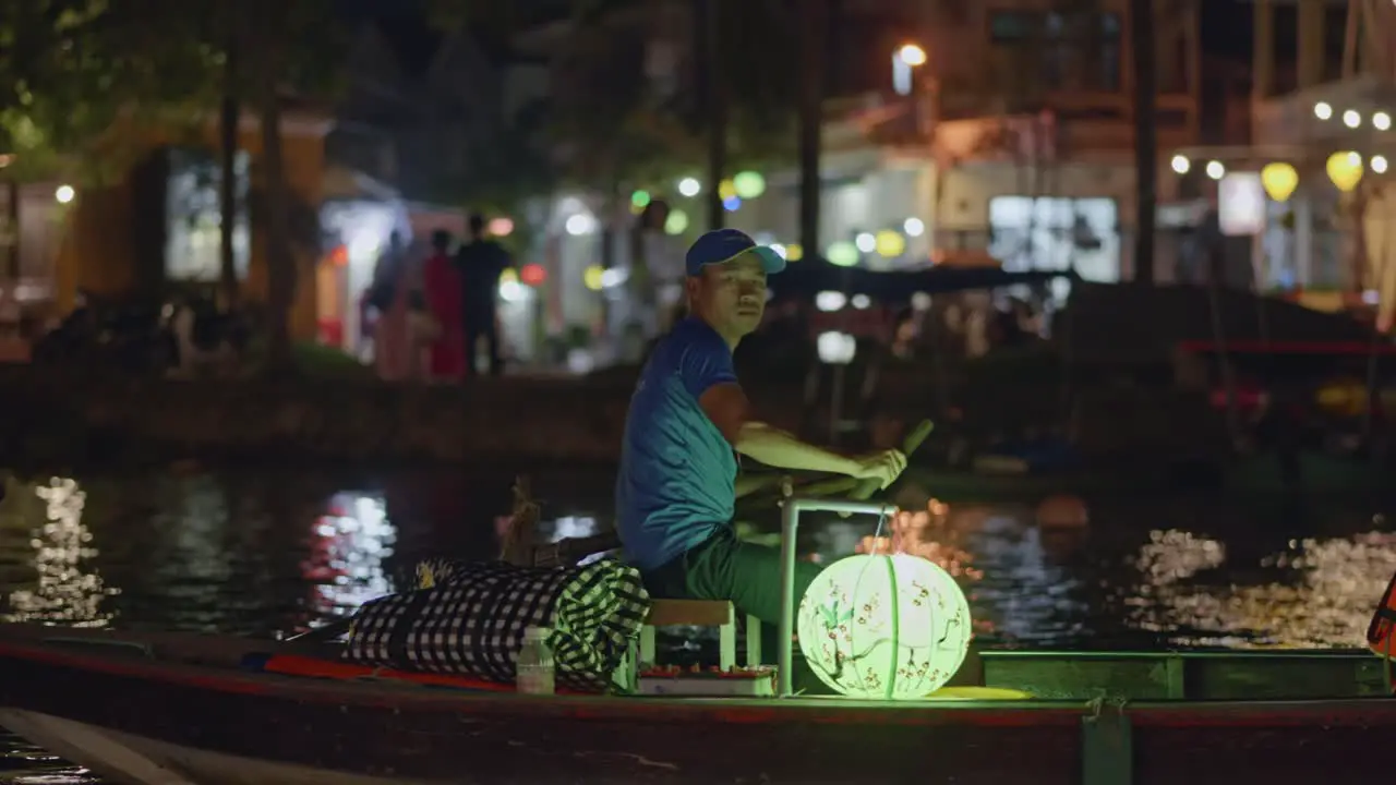 Vietnamese man paddling boat illuminated by lantern at night in Hoi An Vietnam