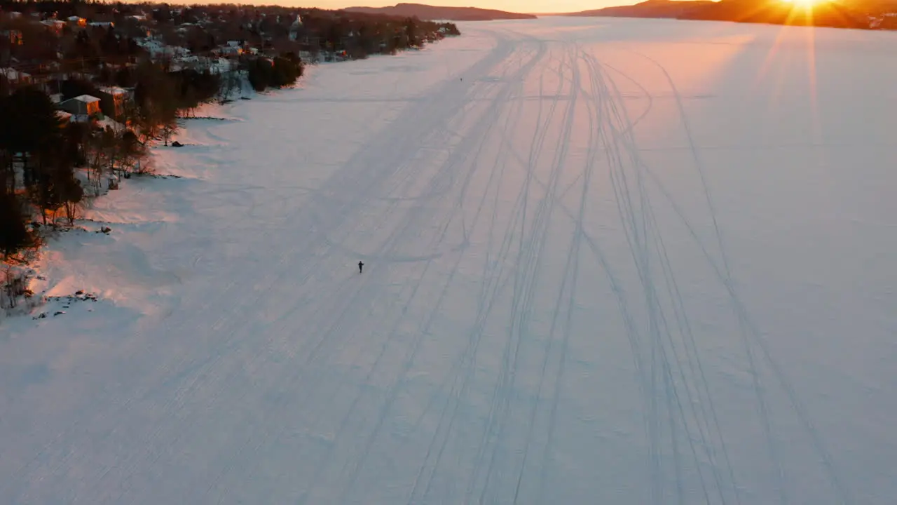 Scenic sunset aerial of a frozen lake as a person snowshoes along the ice and snow