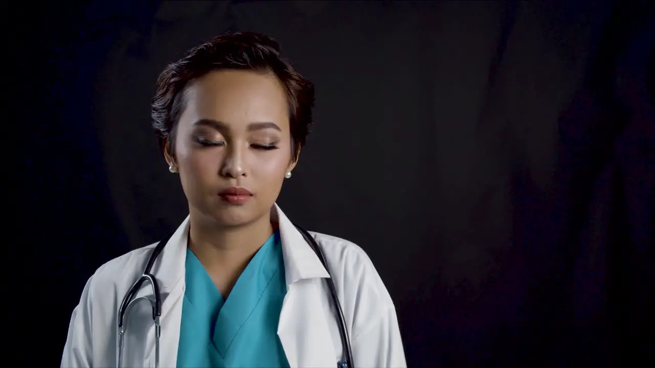 A female doctor or nurse looks at the camera with copy space against black background