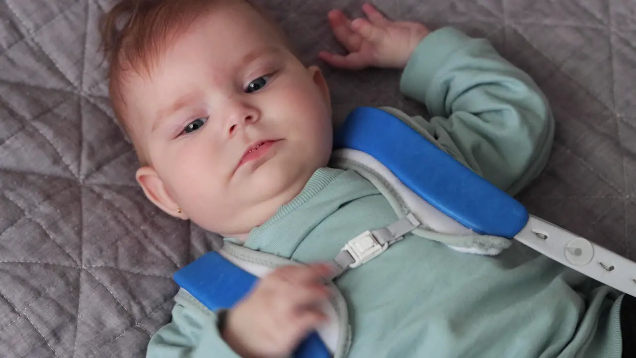 Baby girl in Pavlik Harness to correct Hip Dysplasia lying on blanket