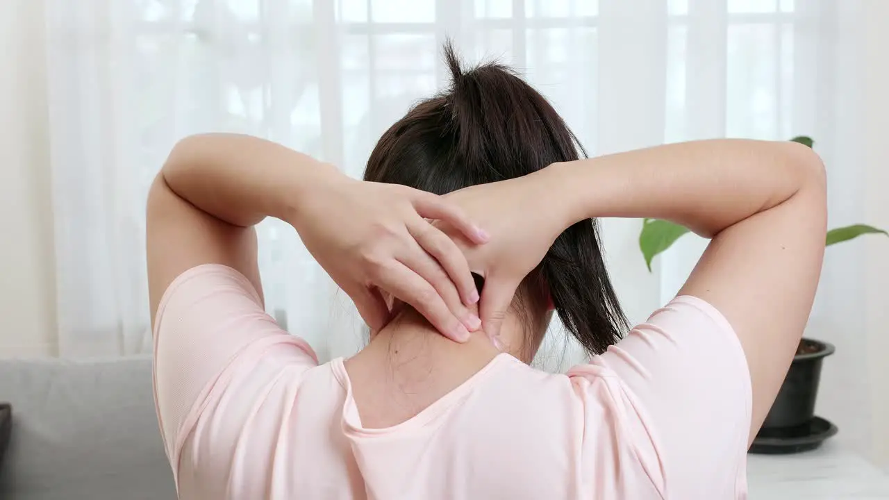 Back view of Asian woman using hands to massage the nape of her neck in physical therapy to reduce pain at work