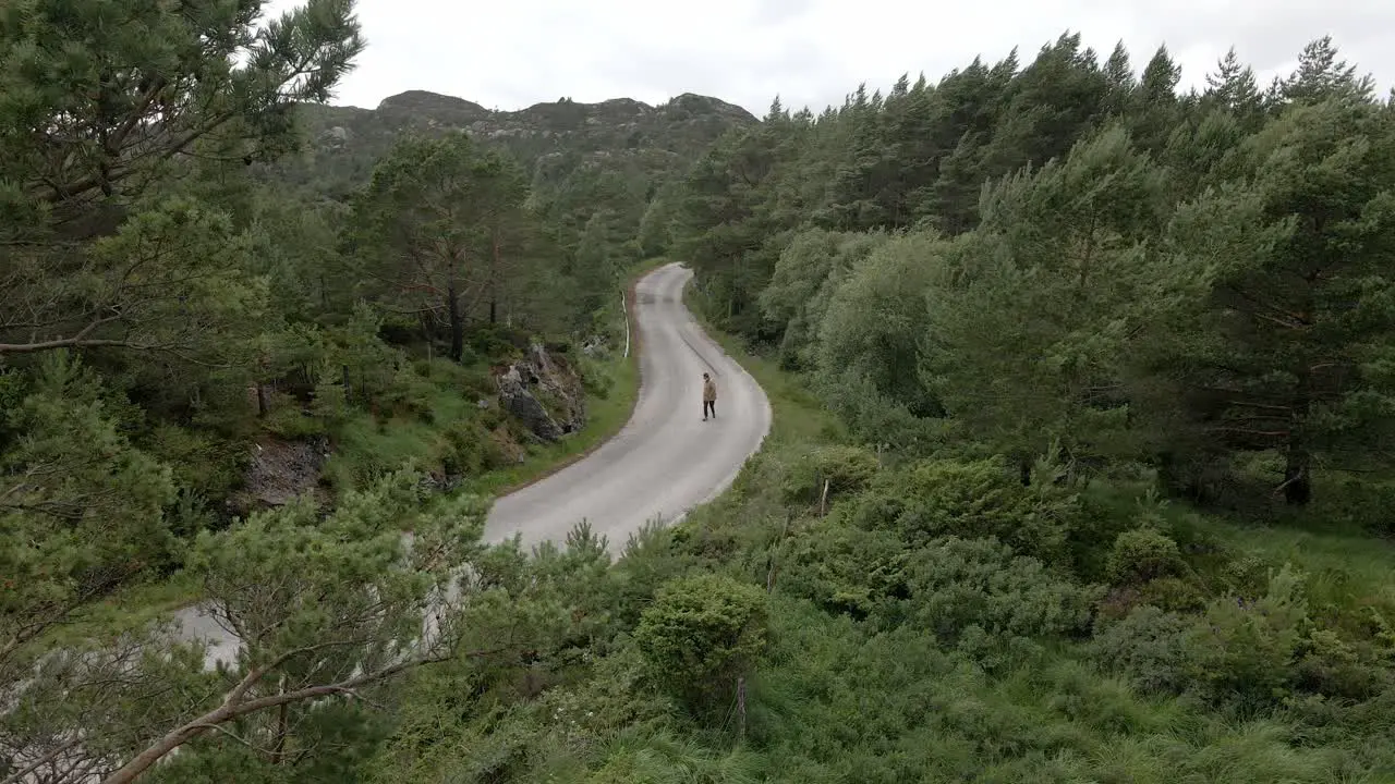 Aerial view of person walking on road in green mountains during cloudy and windy day