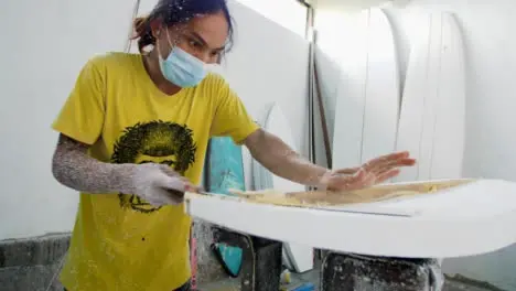 Handheld Wide Shot of Surfboard Shaper Cutting Wood Away from Polystyrene Board