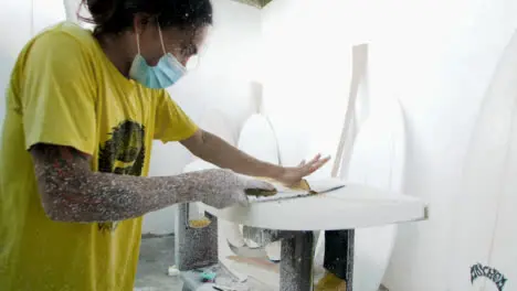 Handheld Wide Shot of Surfboard Shaper Cutting Wood Away from a Polystyrene Board