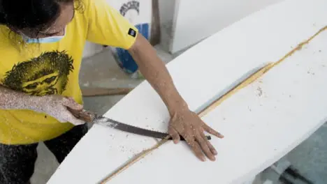 Handheld High Angle Shot of Surfboard Shaper Cutting Wood Away from Polystyrene Board