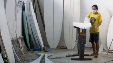 Handheld Wide Shot of Surfboard Shaper Using Power Tool