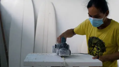 Handheld Wide Shot of a Surfboard Shaper Using Power Tool