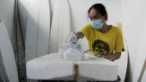 Handheld Wide Shot of a Surfboard Shaper Using a Power Tool On Polystyrene Board