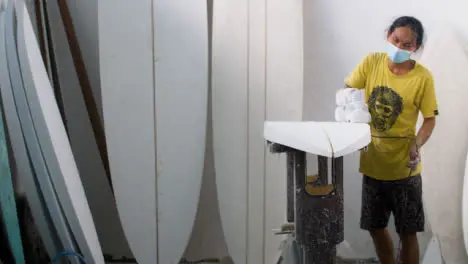 Handheld Wide Shot of a Surfboard Shaper Using a Power Tool