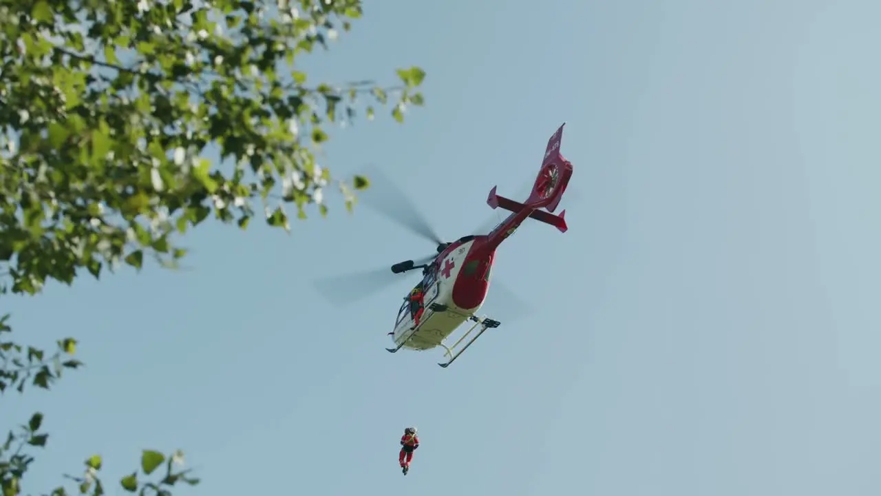 Medical Air Rescue helicopter flying away green leaves in foreground slowmotion