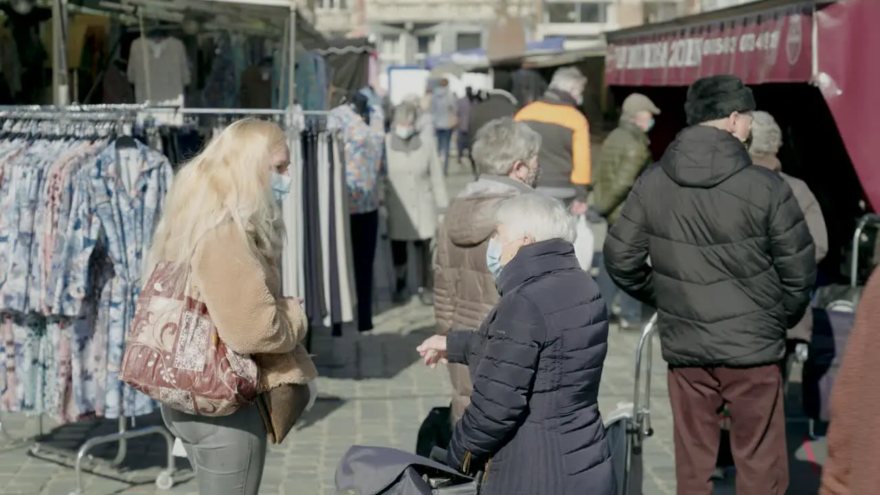 Old woman with medical mask talks with young masked girl at the market as they wait in line for the butcher static shot