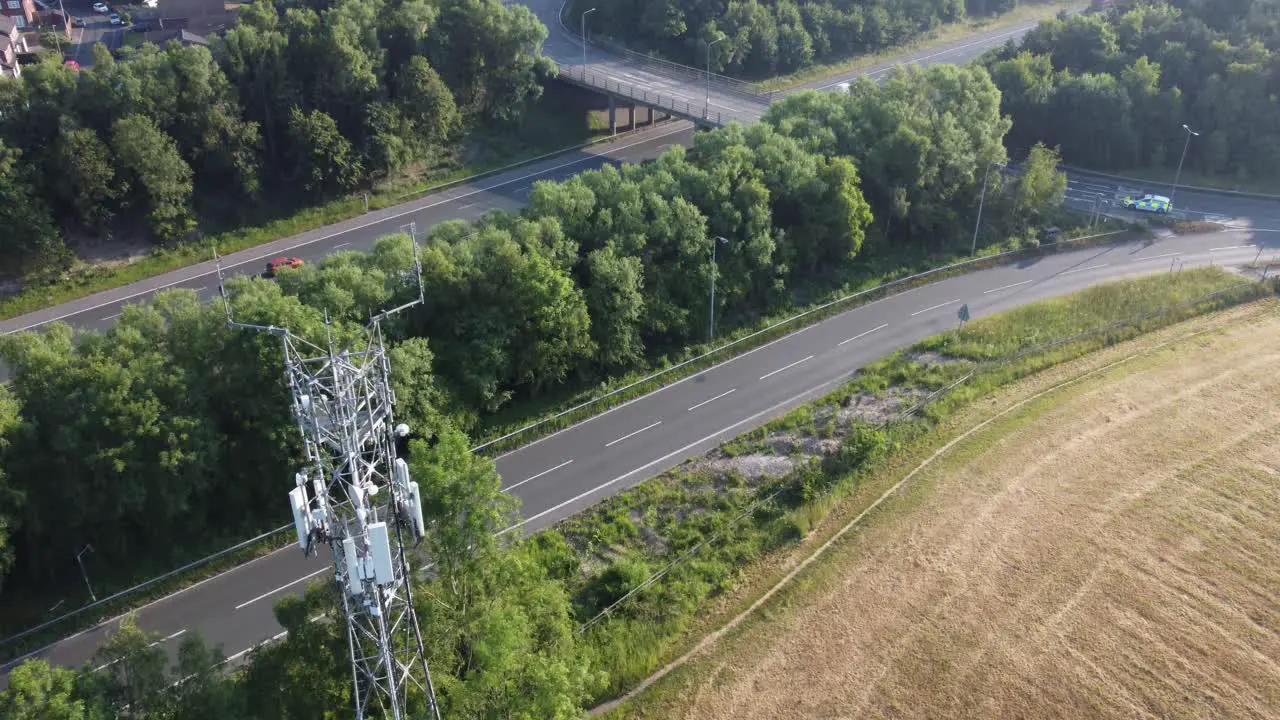 5G broadcasting tower antenna aerial tilt up to British countryside with vehicles travelling on highway background