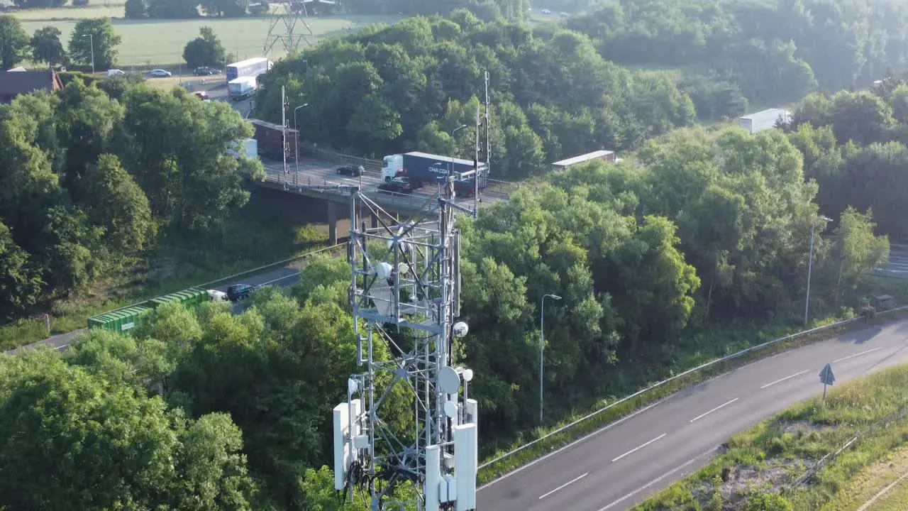 5G broadcasting tower antenna in British countryside with vehicles travelling on highway background aerial tilt up view