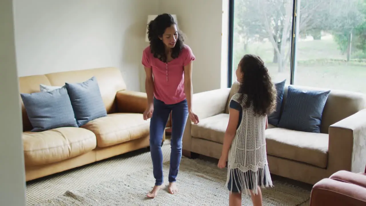 Happy mixed race mother and daughter dancing in living room