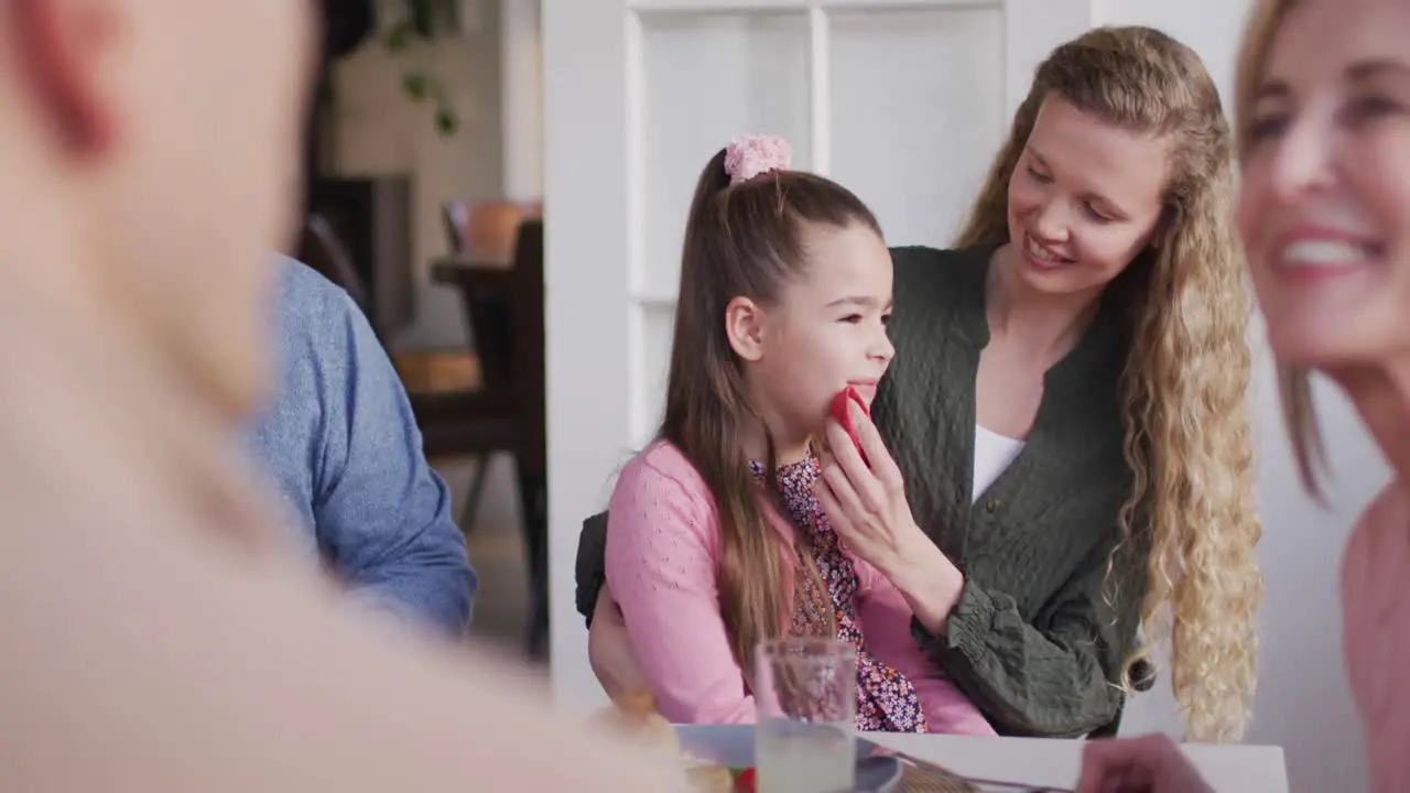 Video of happy caucasian mother cleaning daughter's face at family dinner table