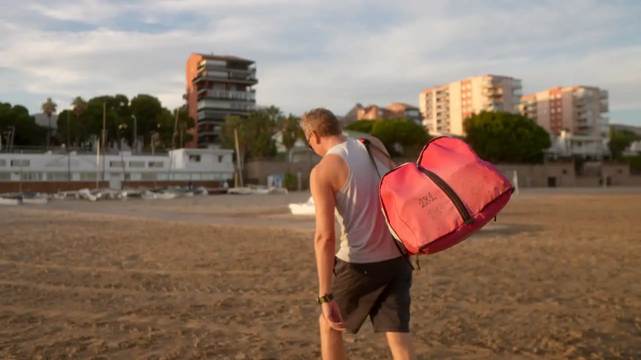 man carrying the sails of a catamaran on the beach at sunset