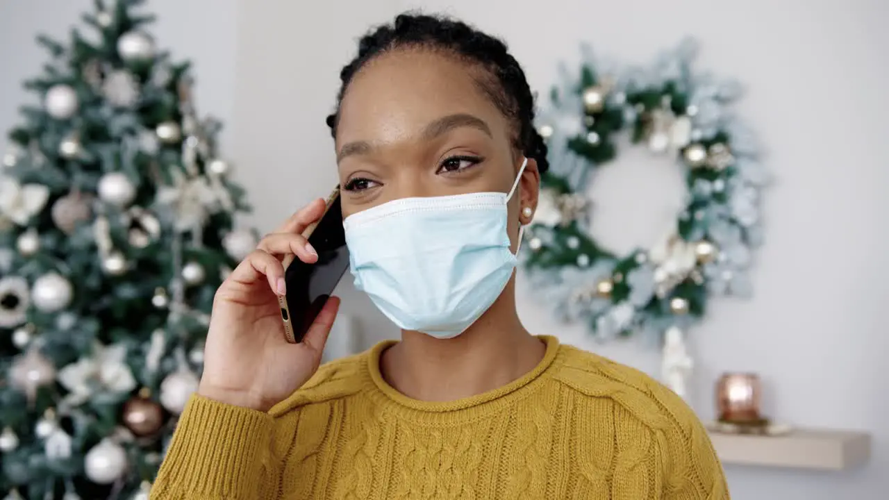 Close Up Portrait Of Happy Young Female In Mask Speaking On Cellphone In Decorated Christmassy Room In Good Mood And Having Good Talk With Friend