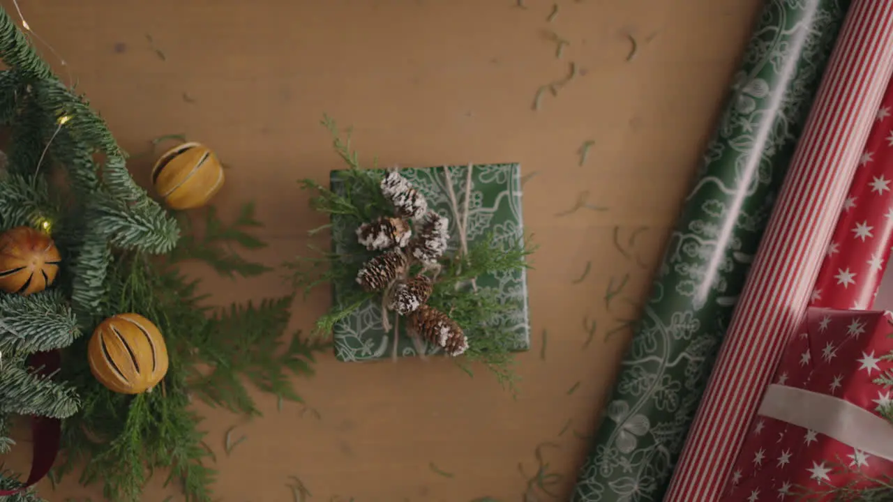 top view of the decorator's desktop Fully visible the table with the decorations Female hands put and finalize Christmas gift wrapped in craftool paper on a wooden table