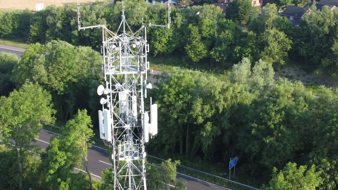 5G cellular tower antenna in British countryside with vehicles travelling on highway background aerial dolly left view