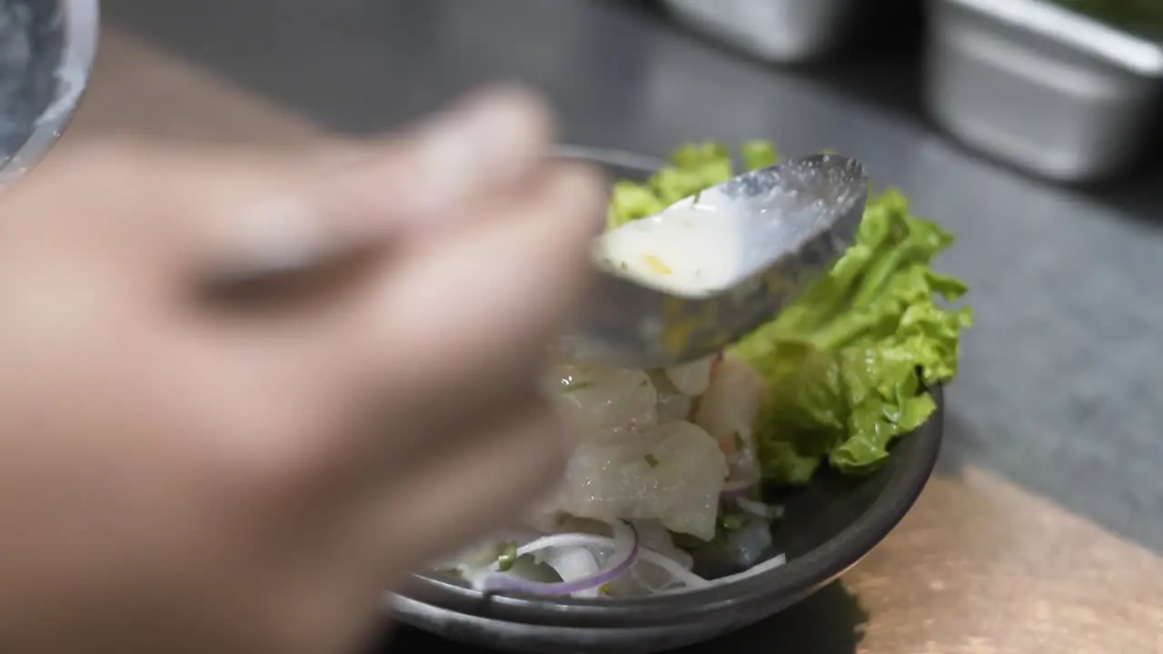 Close-up shot of a hand preparing fresh ceviche with lime onion and lettuce