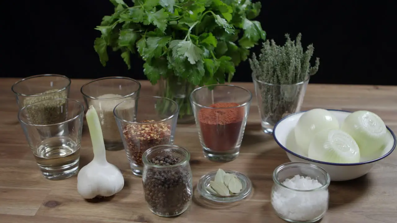 Close up of a wooden table with parsley onion pepper thyme garlic cayenne pepper and rosemary the ingredients for cafe paris butter