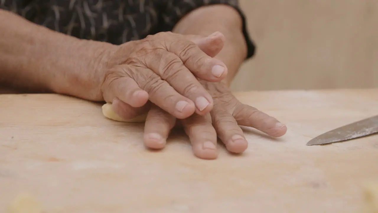 An old woman's hands rolling pasta dough to make into shells in Italy