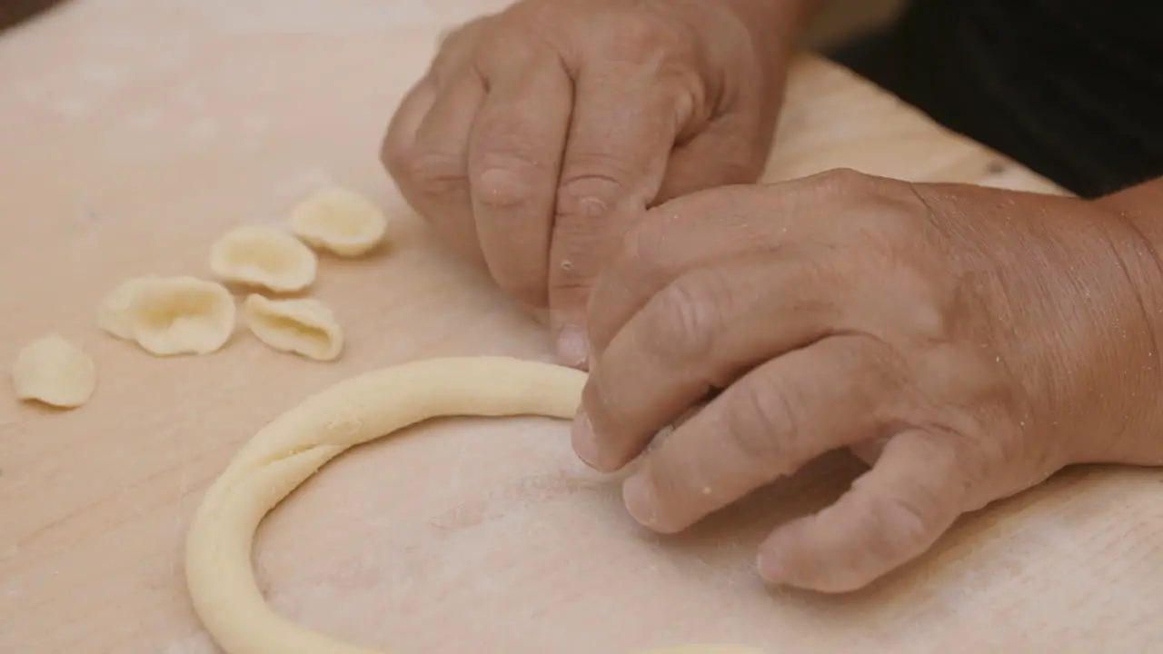 Close up footage of a lady in Bari Italy cutting up a roll of dough to make conchiglie shells pasta