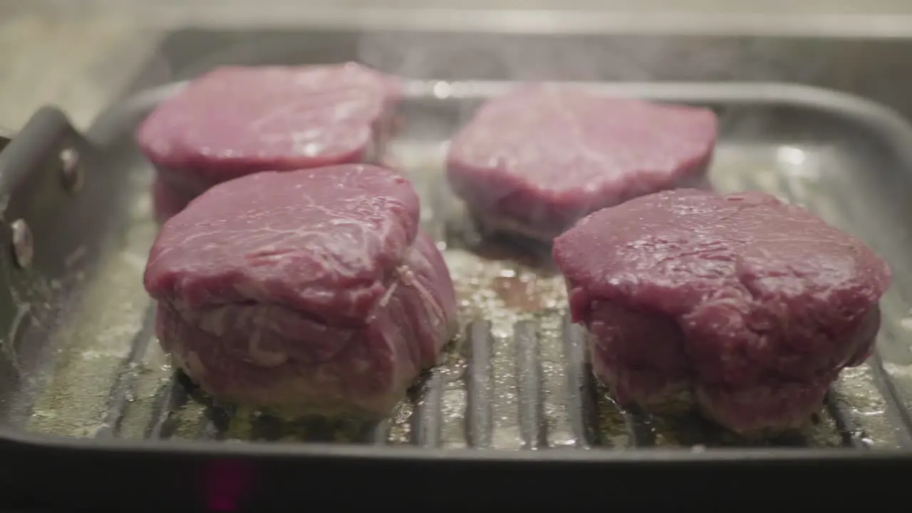 Closeup on four steaks in a frying pan being cooked in oil