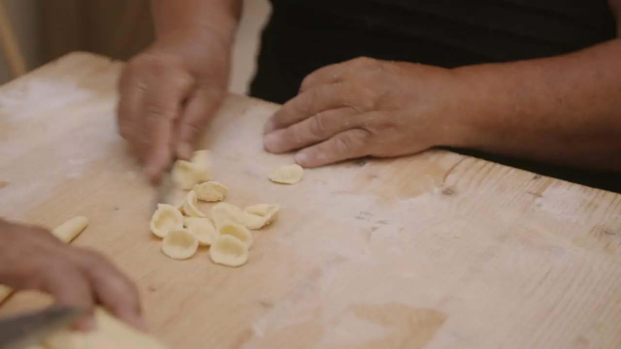 Slow motion footage of an old lady cutting and rolling pasta dough into conchiglie shells in Bari Italy