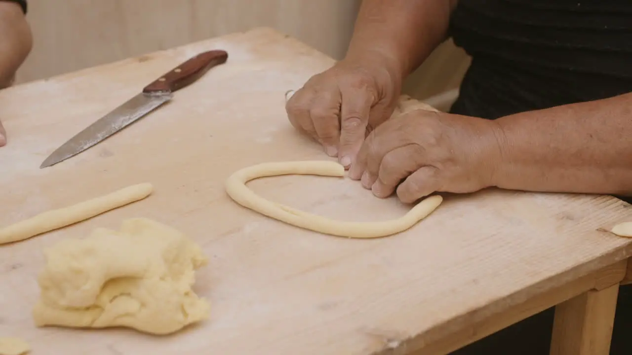 Slow motion footage of a lady in italy rolling dough to make pasta shells and cutting the roll