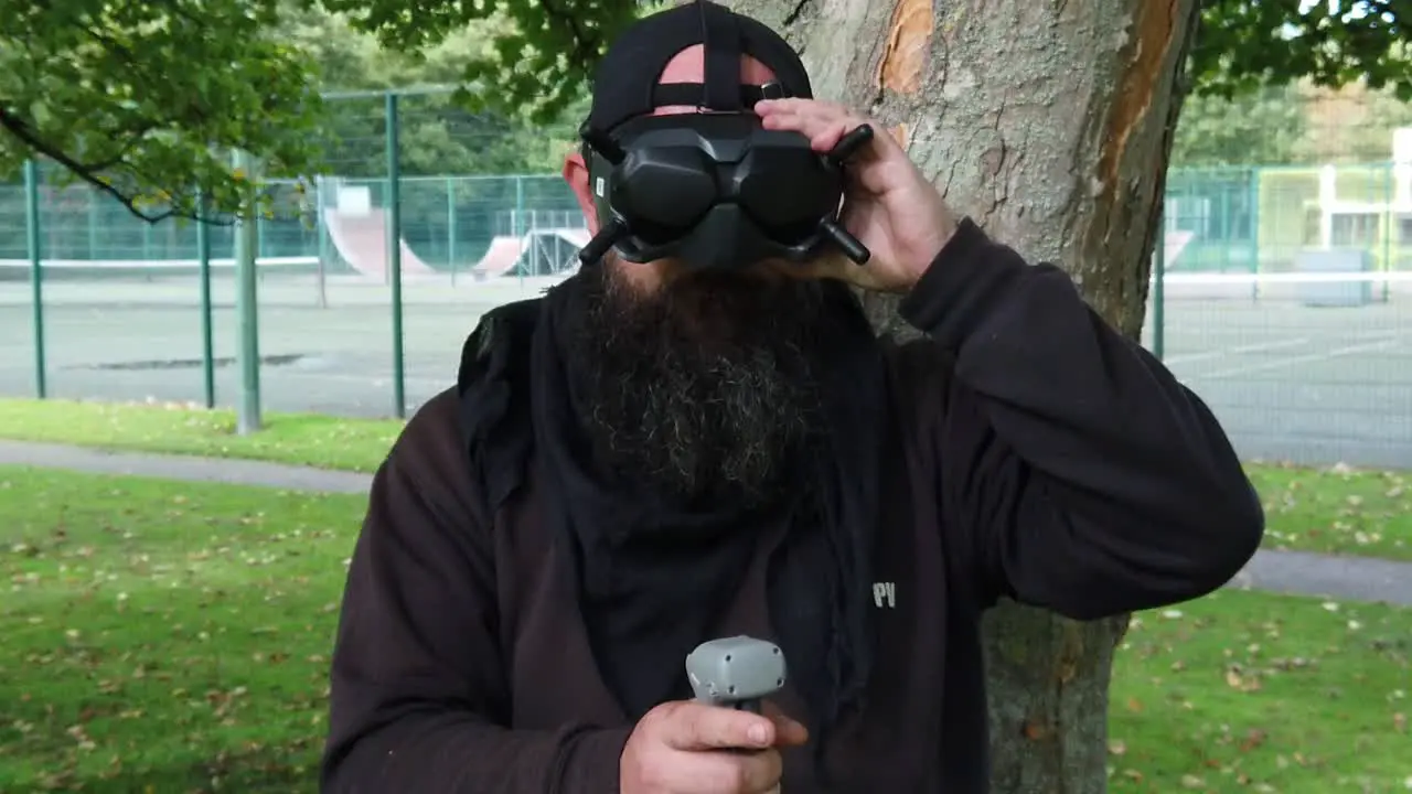 Bearded male wearing FPV goggles tech controlling drone in park with motion joystick