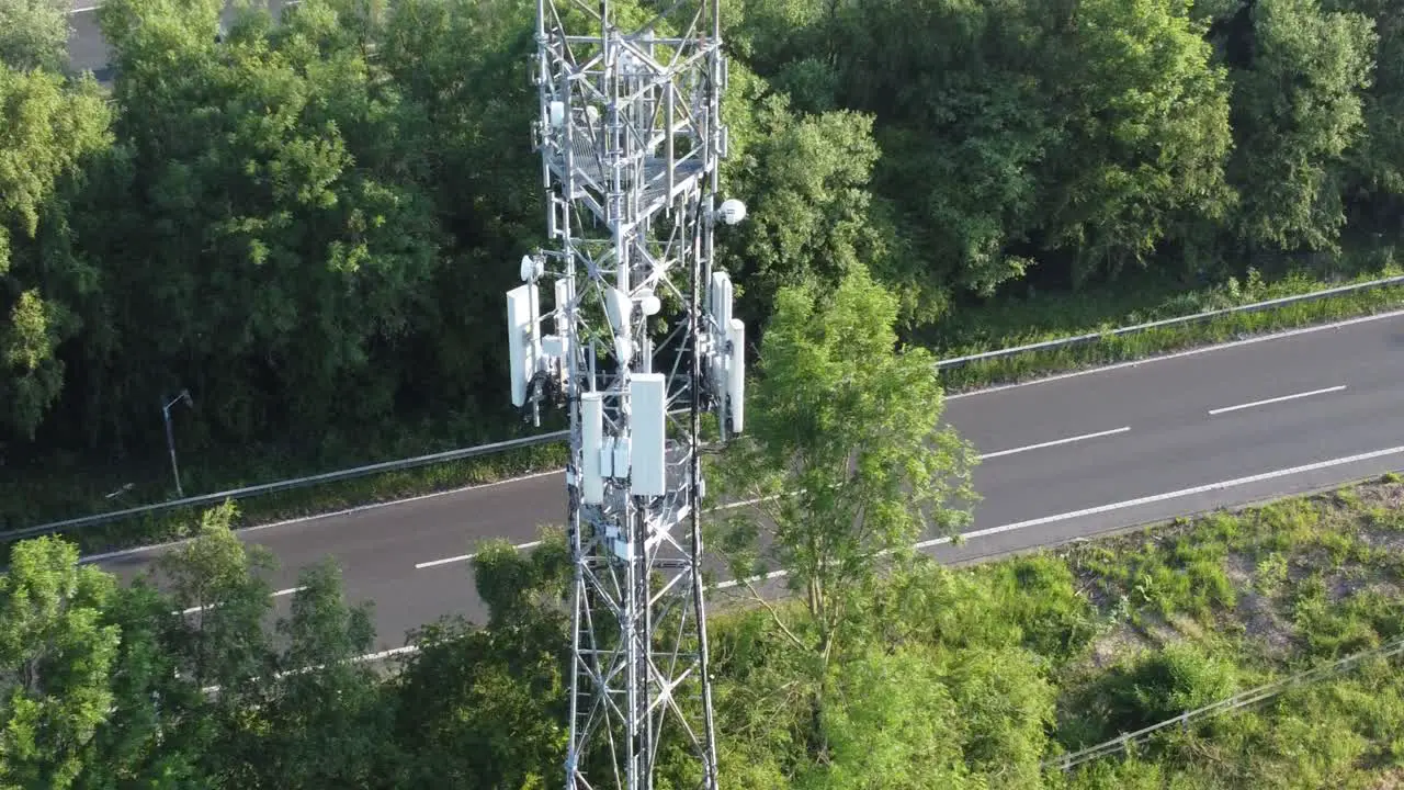 5G broadcasting tower antenna in British countryside with vehicles travelling on highway background aerial orbit view left