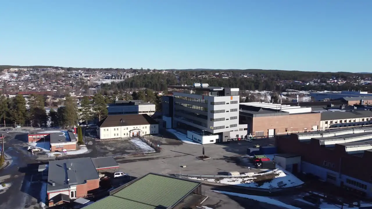 Distant rotating aerial view of Kongsberg Defence and Aerospace headquarter with logo Technology company Manufacturing buildings to the right and Kongsberg city in background