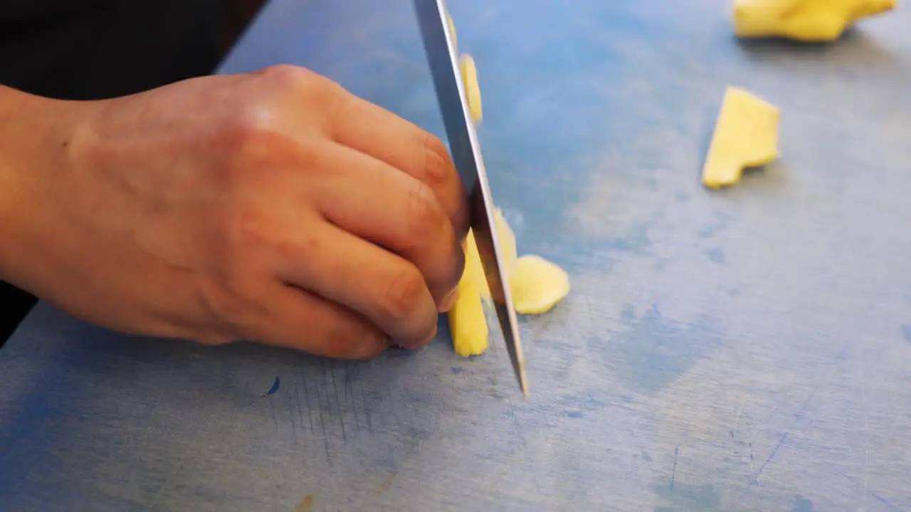 Cutting ginger into small pieces on blue cutting board for Asian noodles in a sushi restaurant by a chef