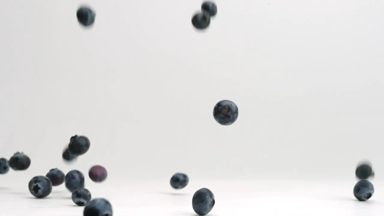 Blueberries falling and bouncing in slow motion onto white studio backdrop in 4k