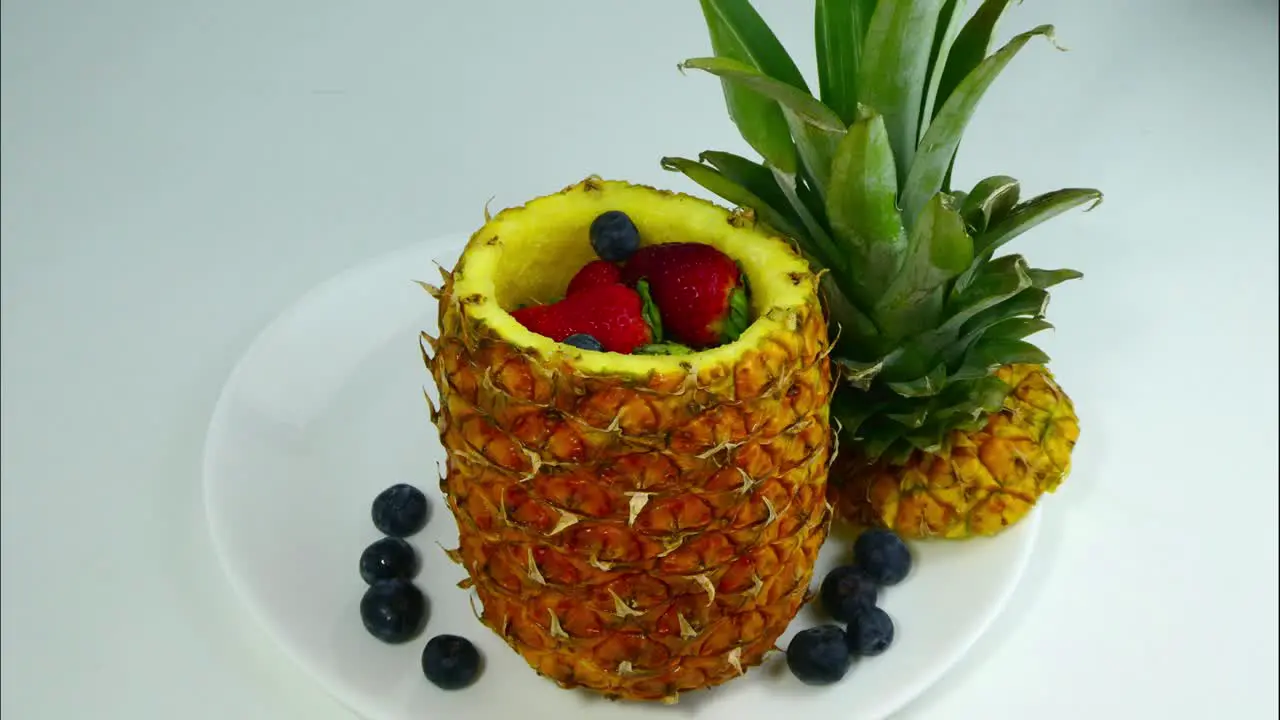 Stop motion of a pineapple that opens and from which strawberries and blueberries are coming out