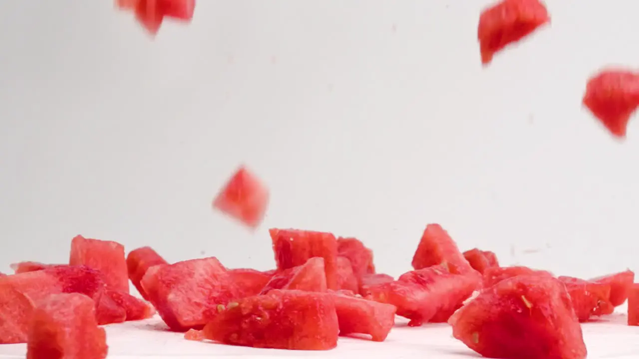 Pink juicy diced watermelon cube pieces falling and bouncing on white table top in slow motion with juice and seeds splattering everywhere