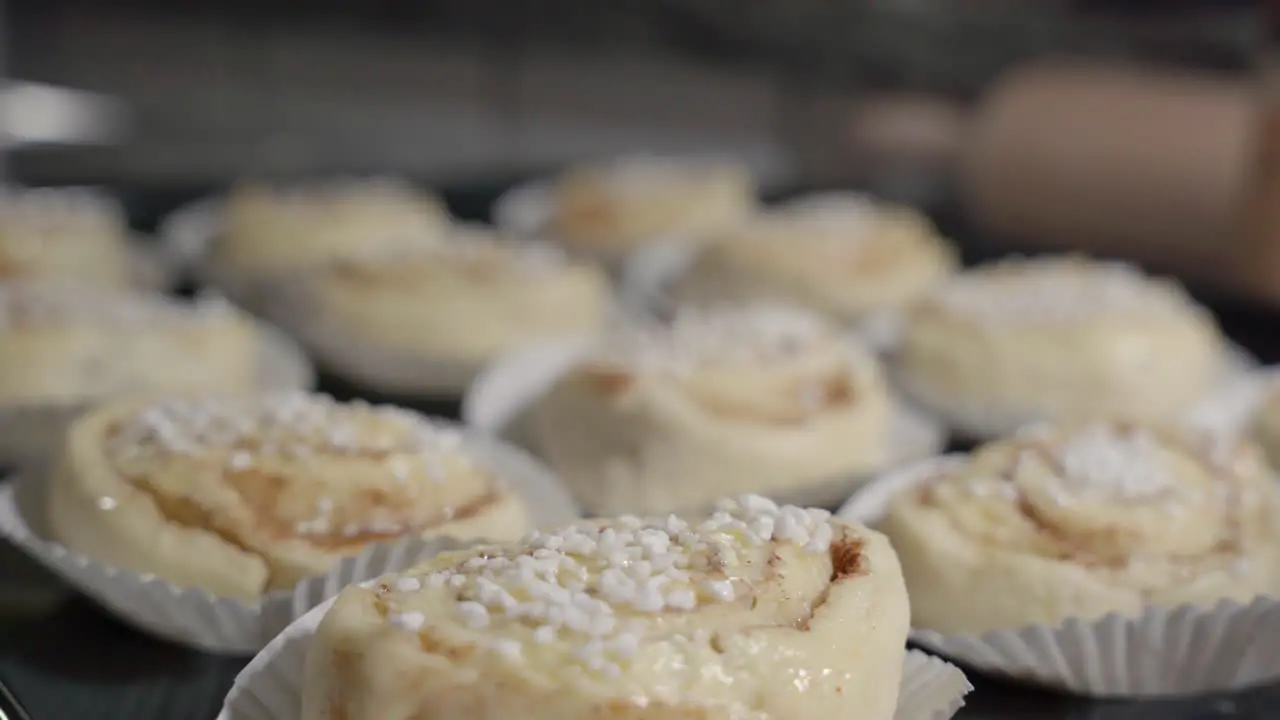 Static close up of cinnamon buns with focus pulling and baking utensils in the background