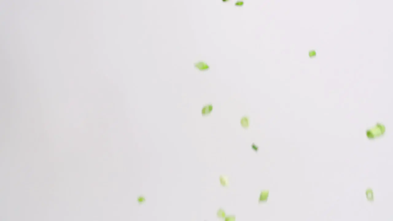 Diced and chopped green onion pieces raining down on white backdrop in slow motion