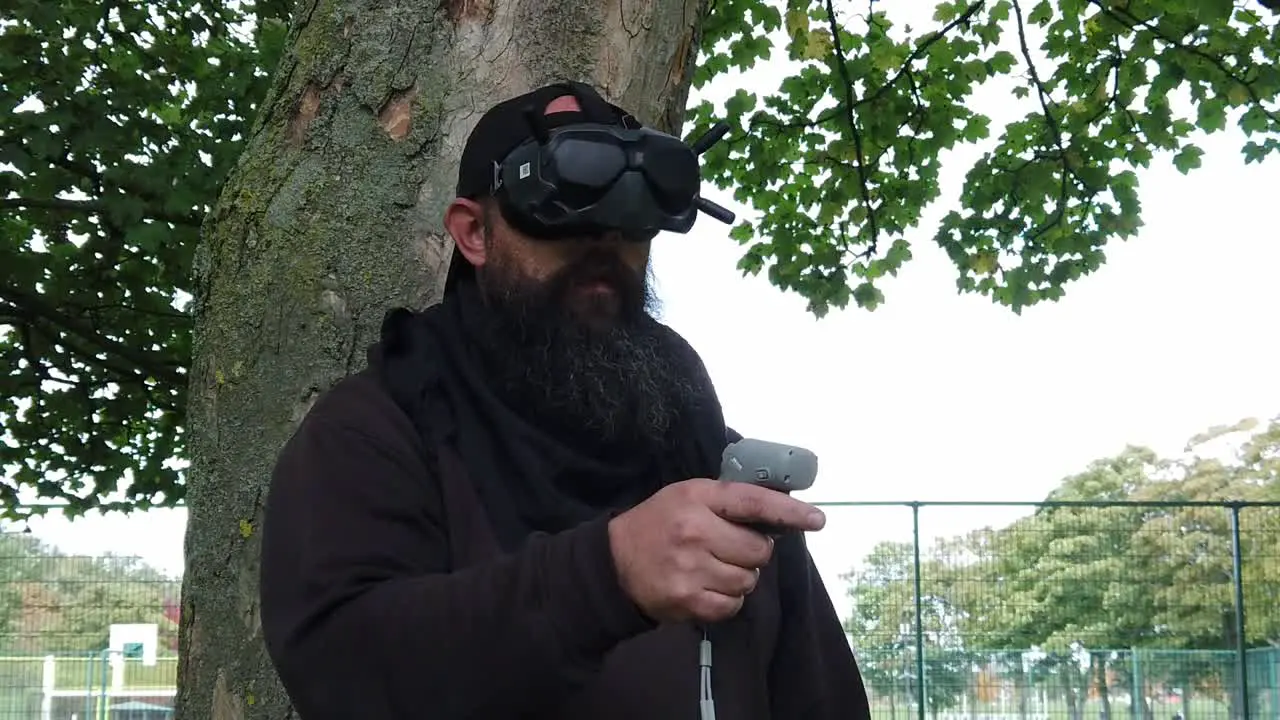 Bearded male wearing FPV goggles controlling drone in park with motion joystick