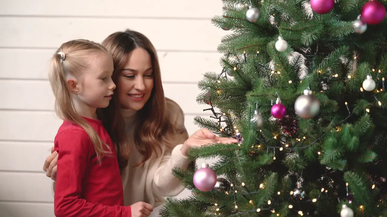 Mother With Her Daughter Hanging Christmas Ornaments On Christmas Tree