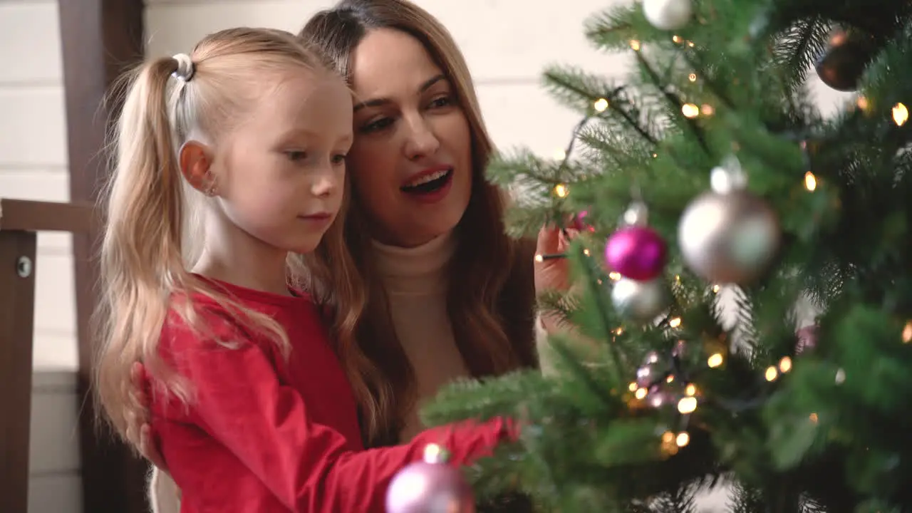 Mother With Her Daughter Hanging Christmas Ornaments On Christmas Tree 2