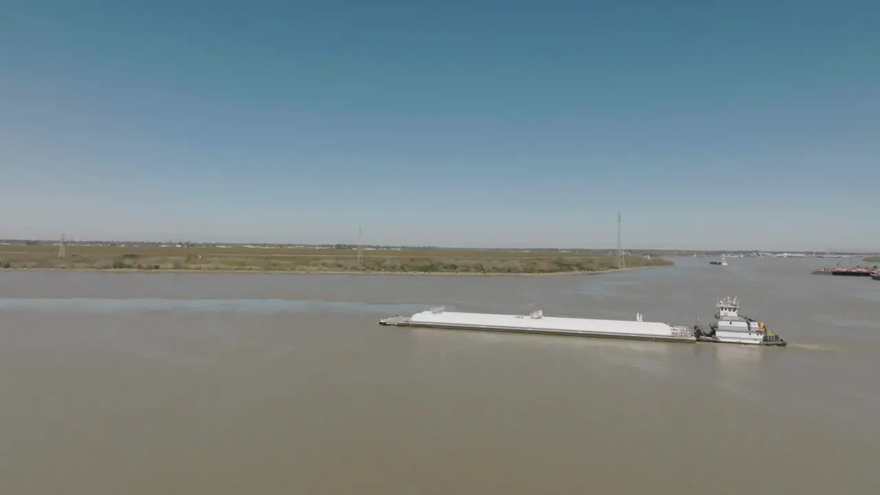 An aerial view of a tugboat pushing a barge up the Houston Ship Channel under the clear blue skies of Houston Texas