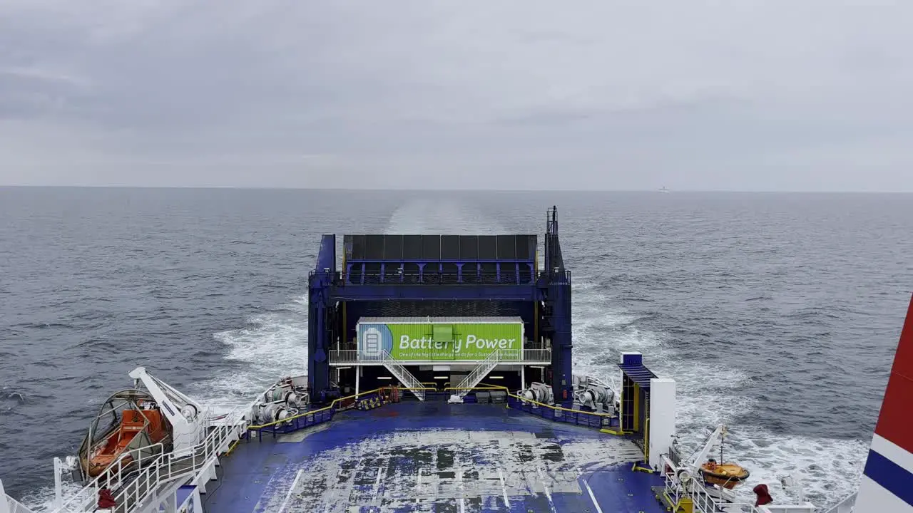 View of the end of a car ferry sailing across the sea under an overcast sky blue and white ship