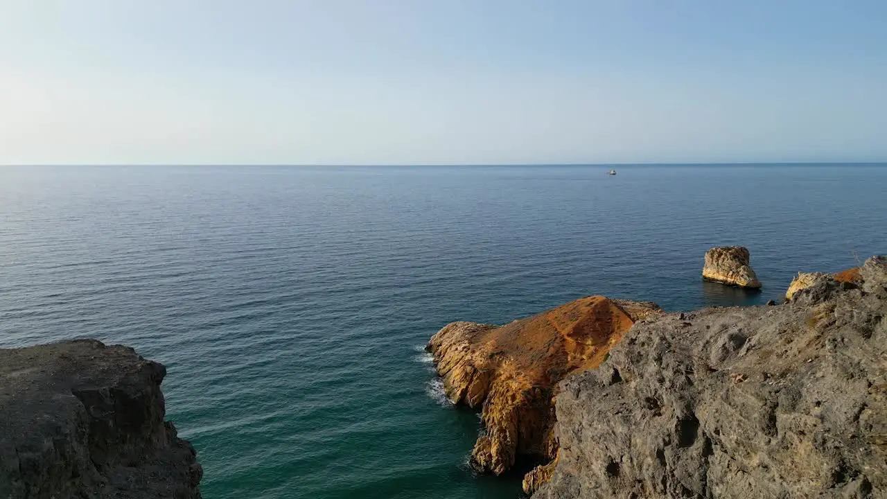 A panoramic aerial view captures a majestic cliff a rugged rocky beach and a distant cargo ship on the horizon