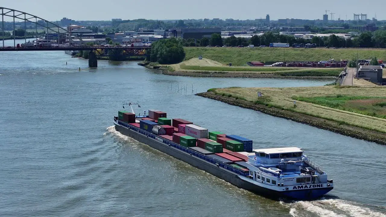 Aerial drone circling around large cargo ship carrying shipping containers approaching bridge