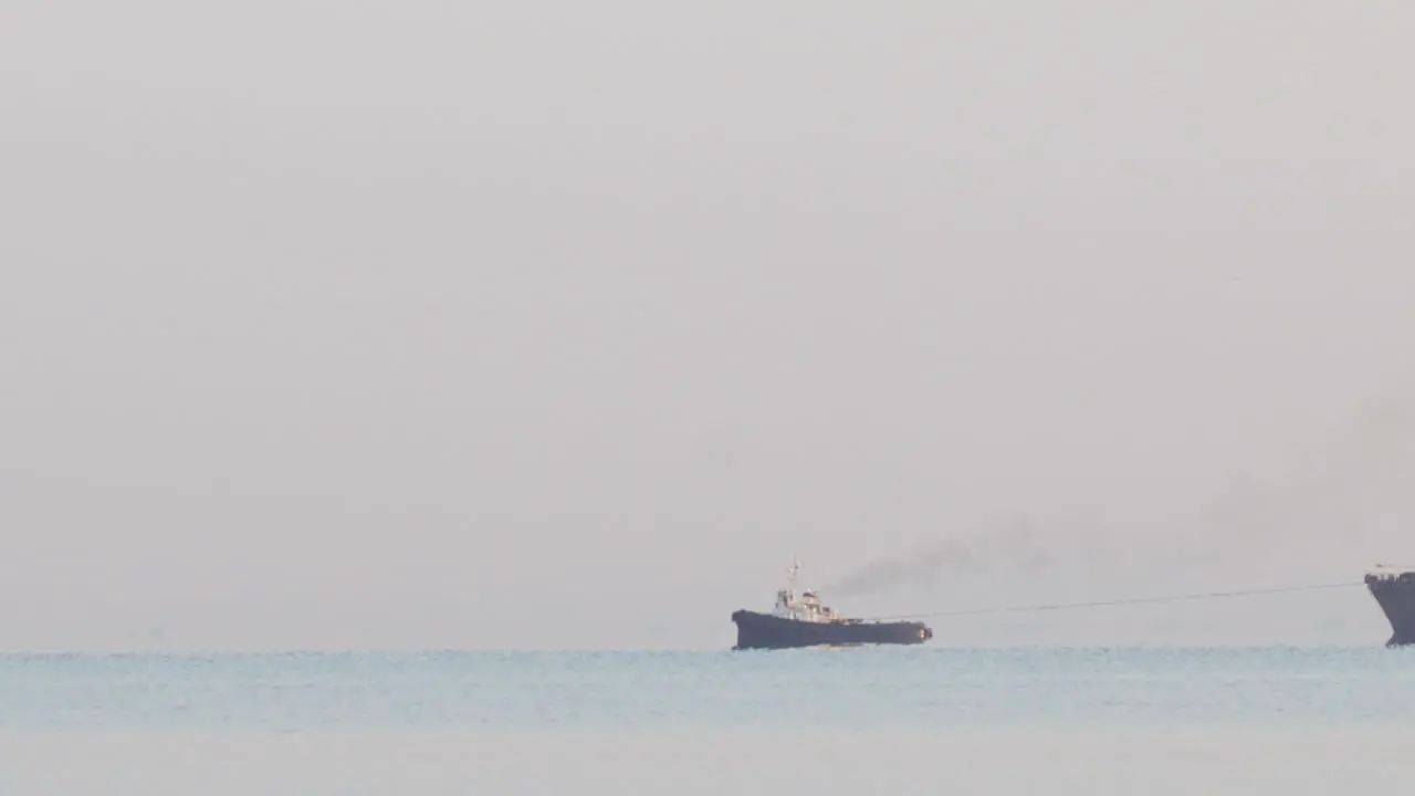 Tugboat tugging a large barge in an overcast day