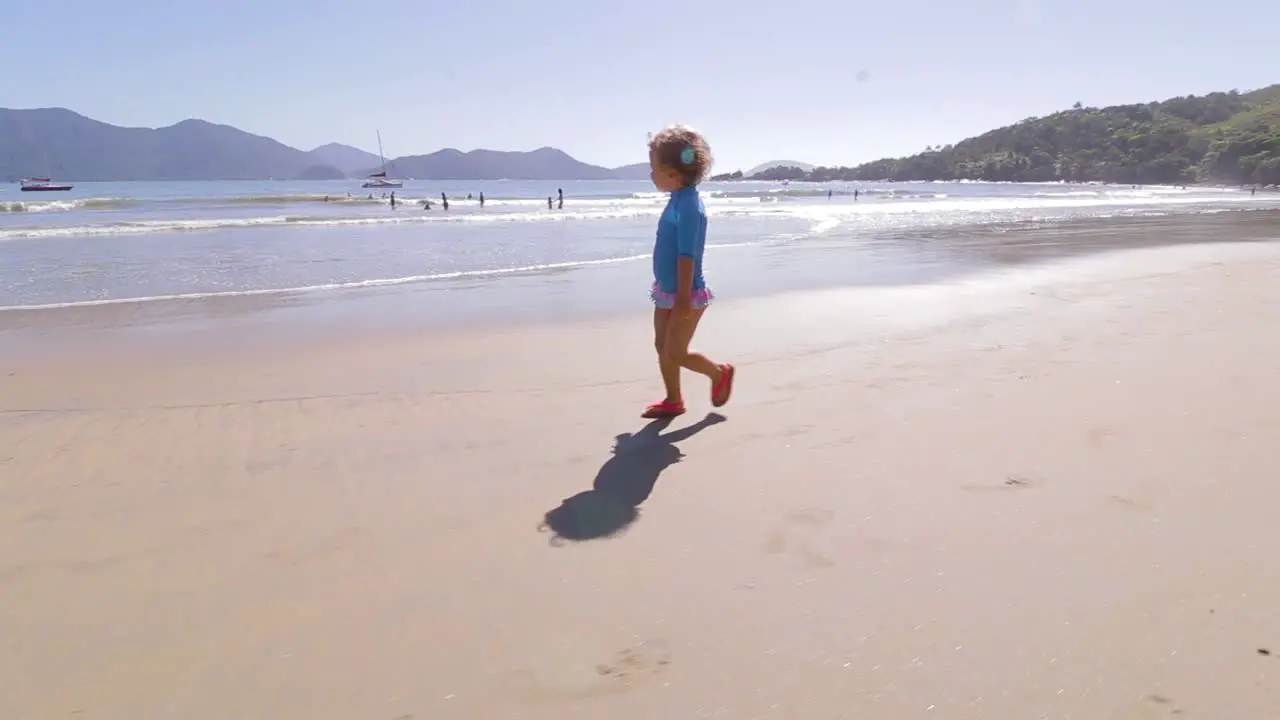 camera orbiting around young cute girl running freely on the beach with mountains background and calm sea and clear sand contemplating the environment