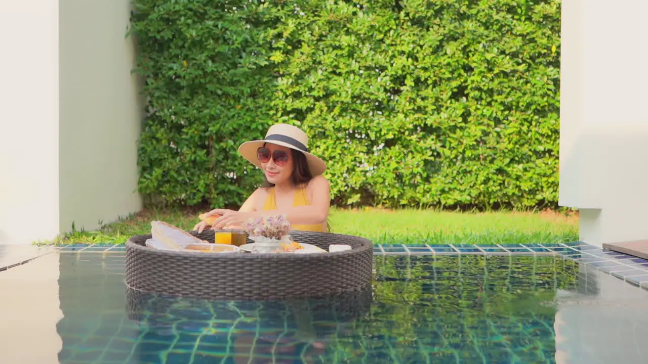 Woman with floating breakfast tray in swimming pool luxury vacation